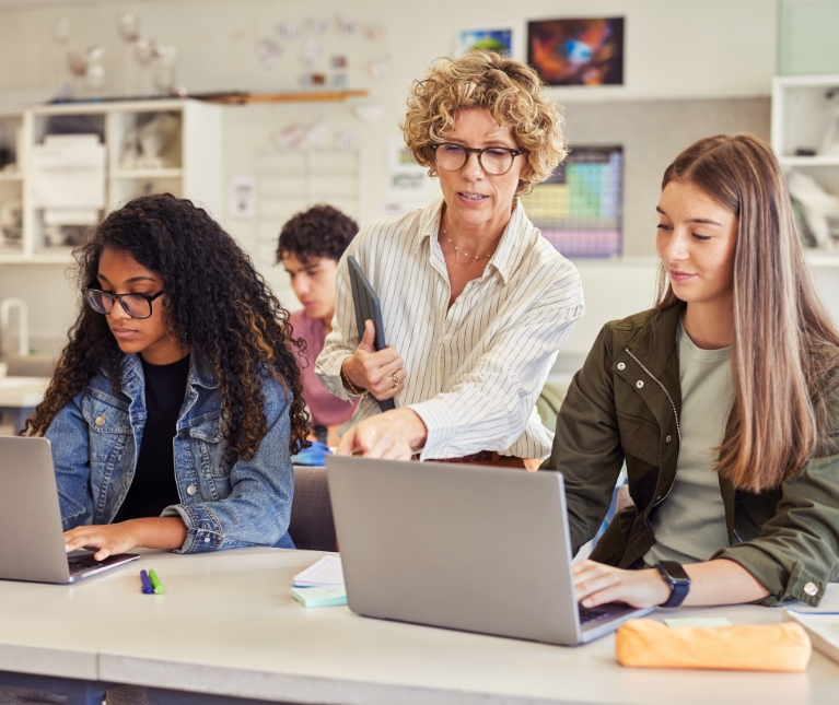 Teacher assisting students using laptops