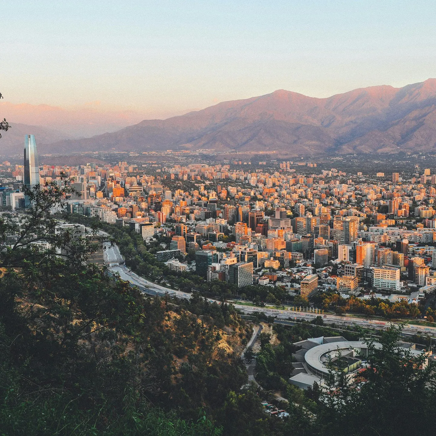 Cityscape of a densely built urban area with tall buildings and mountains in the background during sunset.