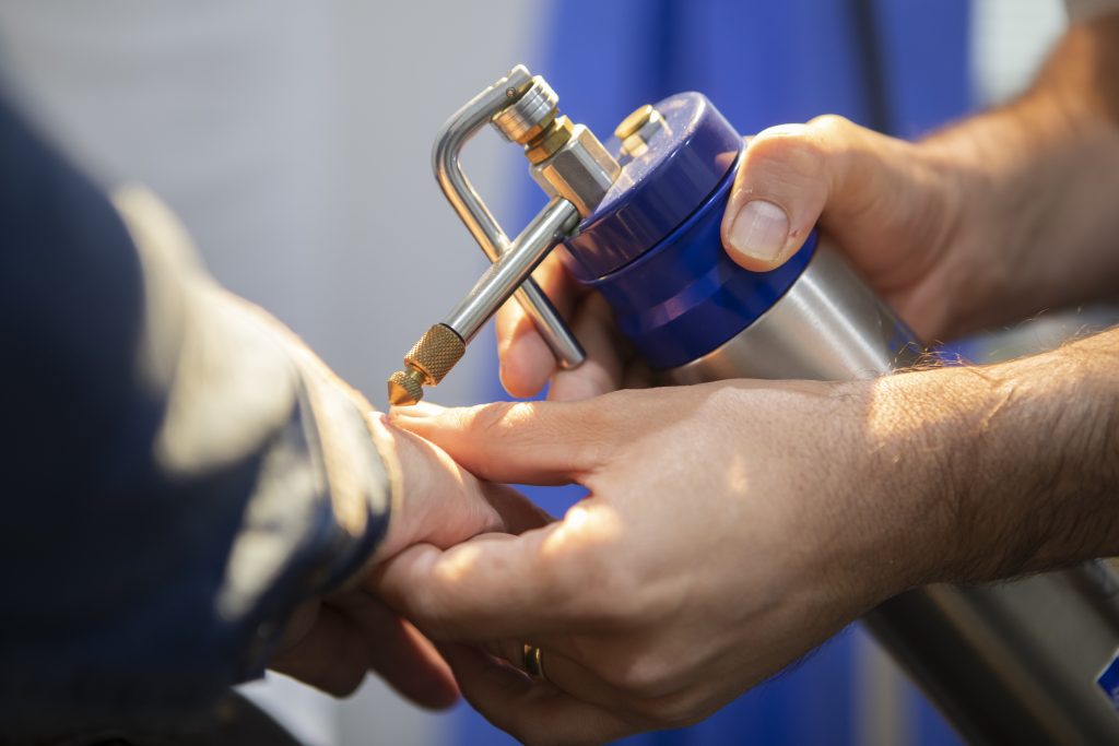 Close-up of a hand holding a small airbrush tool spraying another person's finger.