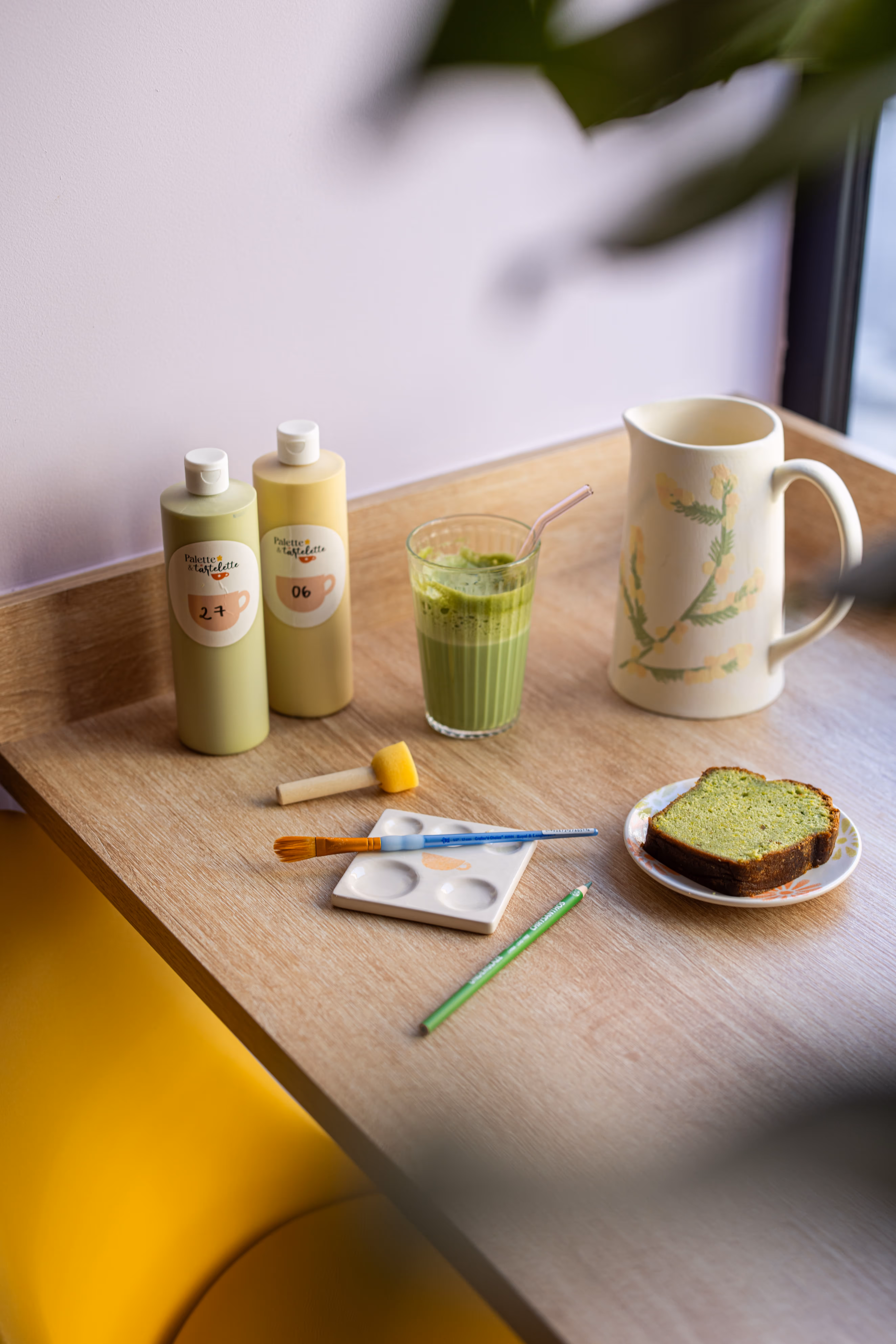 Plateau avec un matcha latte, une tranche de banana bread, des peintures et une pièce en céramique