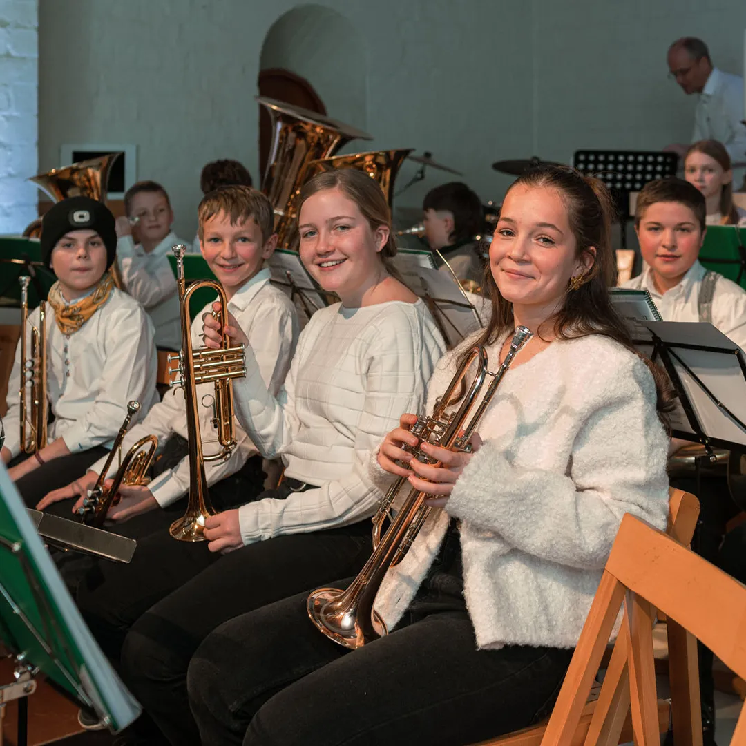 Jugendliche mit verschiedenen Instrumenten im Orchester sitzen vor ihren Notenständern.