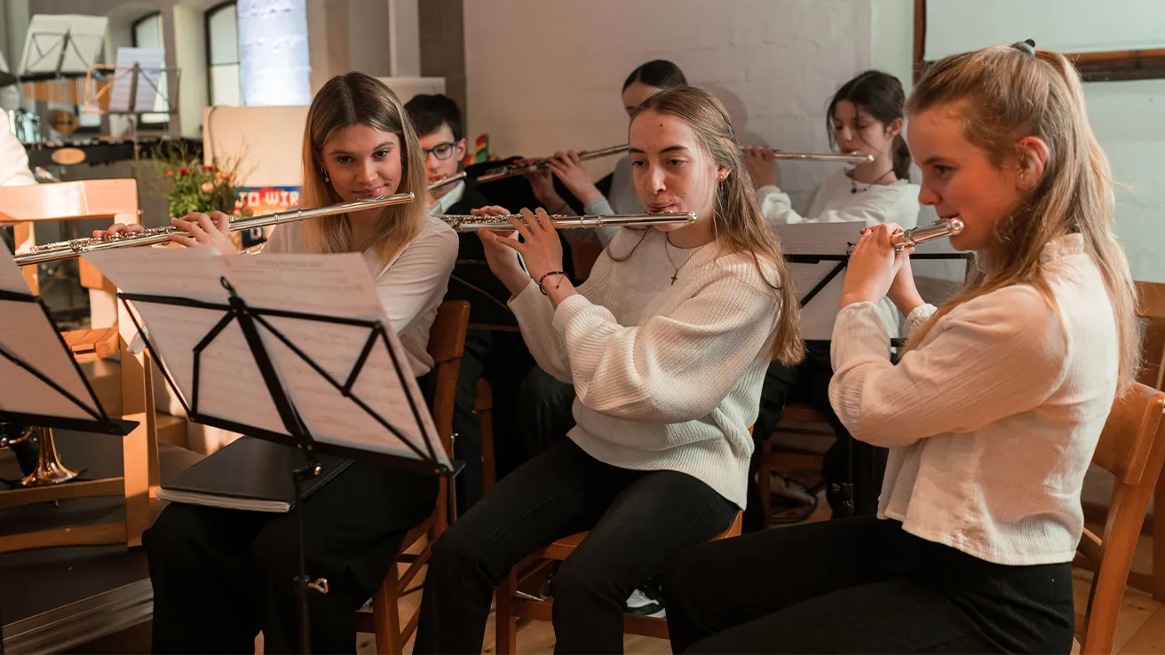 Drei Mädchen mit Querflöten spielen im Orchester vor Notenständern.