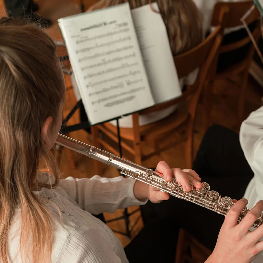 Mädchen mit Querflöte bei einer Musikprobe. Im Hintergrund ein Notenständer mit geöffneter Partitur.