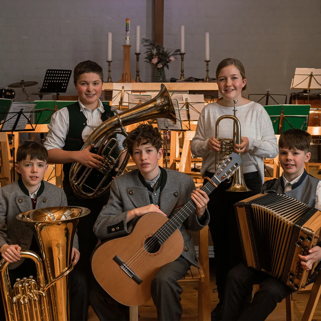Kinder mit verschiedenen Instrumenten vor einem Altar und Notenständern.