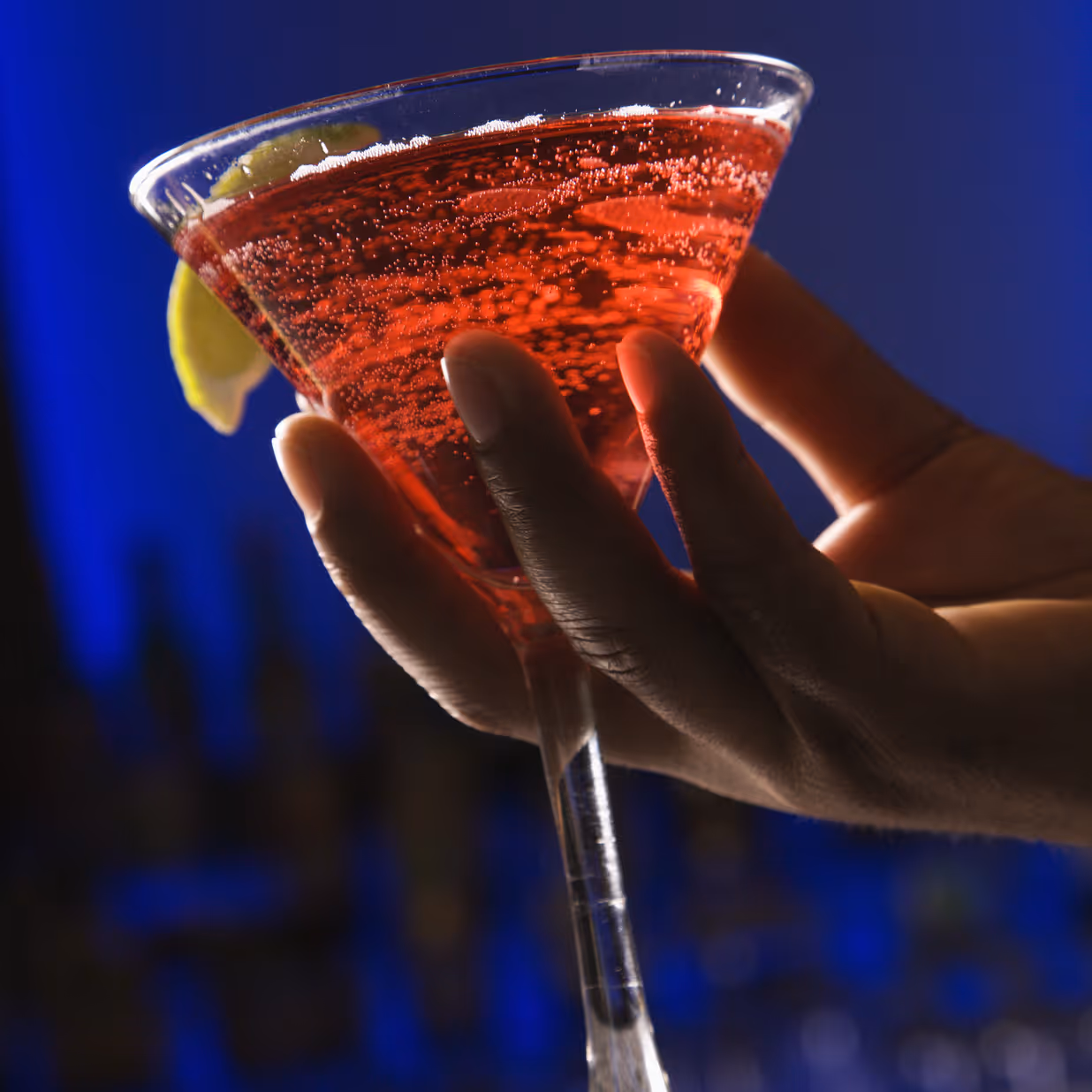 Hand holding a vibrant red Madame Mocktail zero-proof drink against a bold blue background