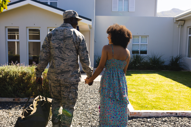 veteran soldier in camouflage holding wife hand walking towards new house with va loan