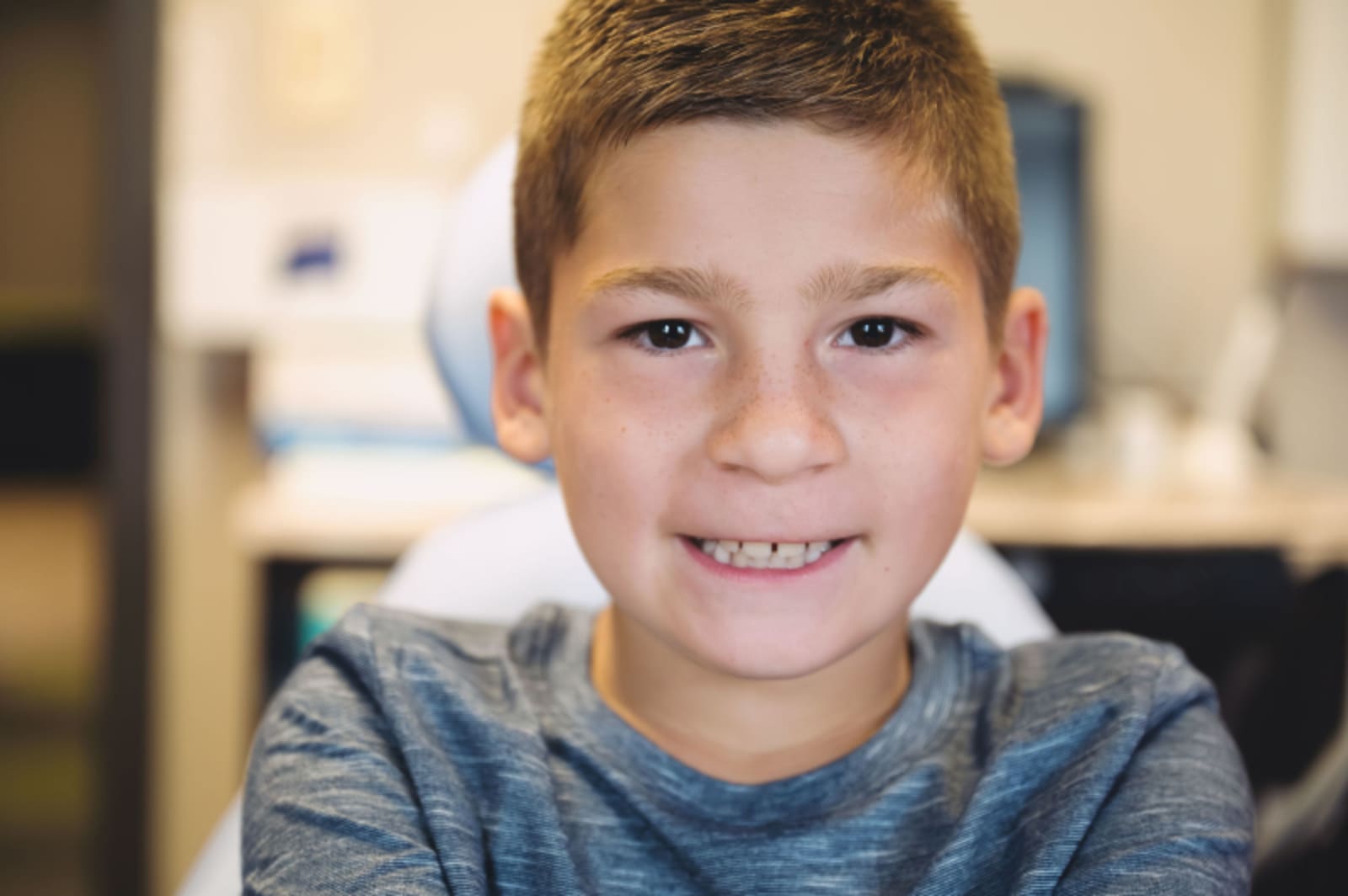 Smiling young boy in a casual grey shirt in a dental office setting.
