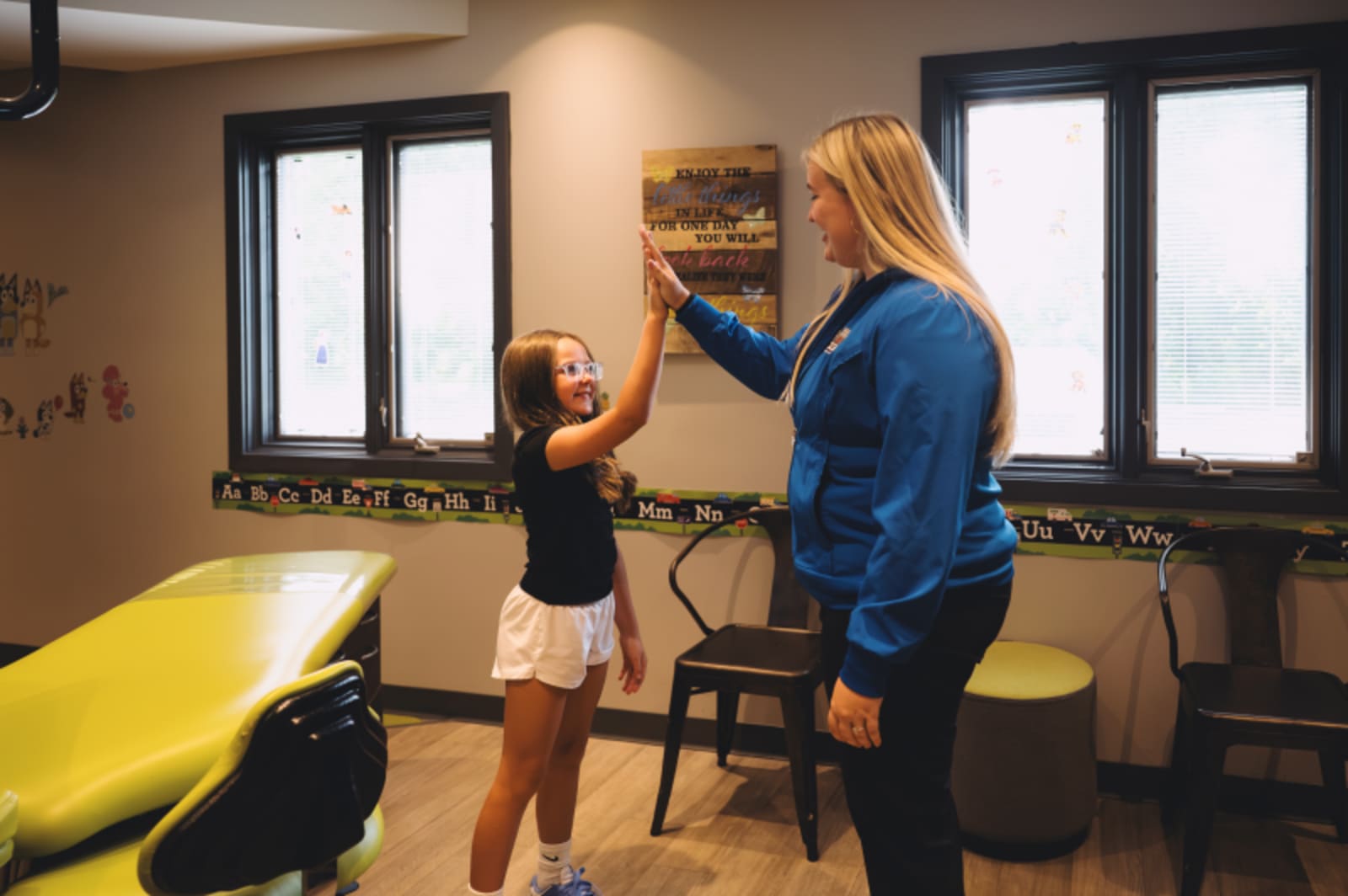 Pediatric dentist in blue scrubs working with young patient in modern dental treatment room with yellow equipment.