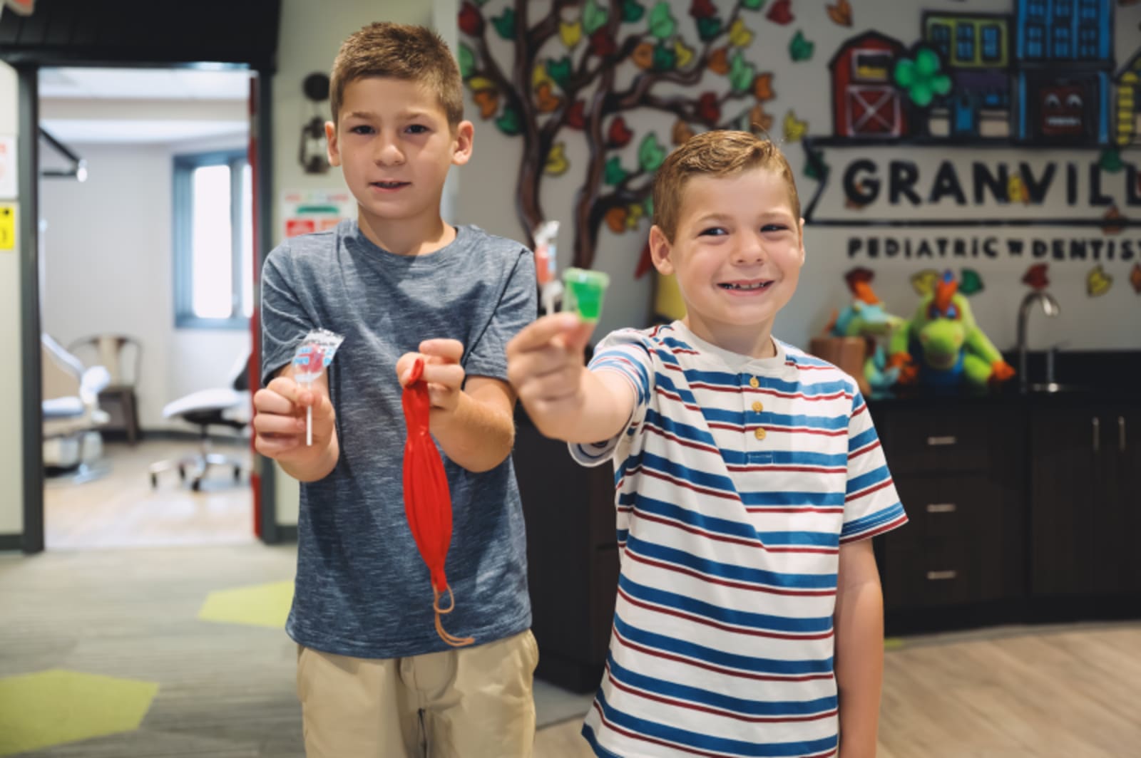 Two young children holding toothbrushes in a bright dental office setting.
