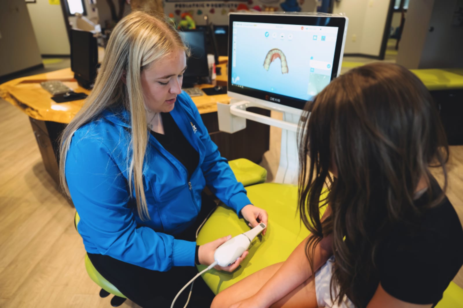 Dentist in blue jacket examining young child at dental computer workstation