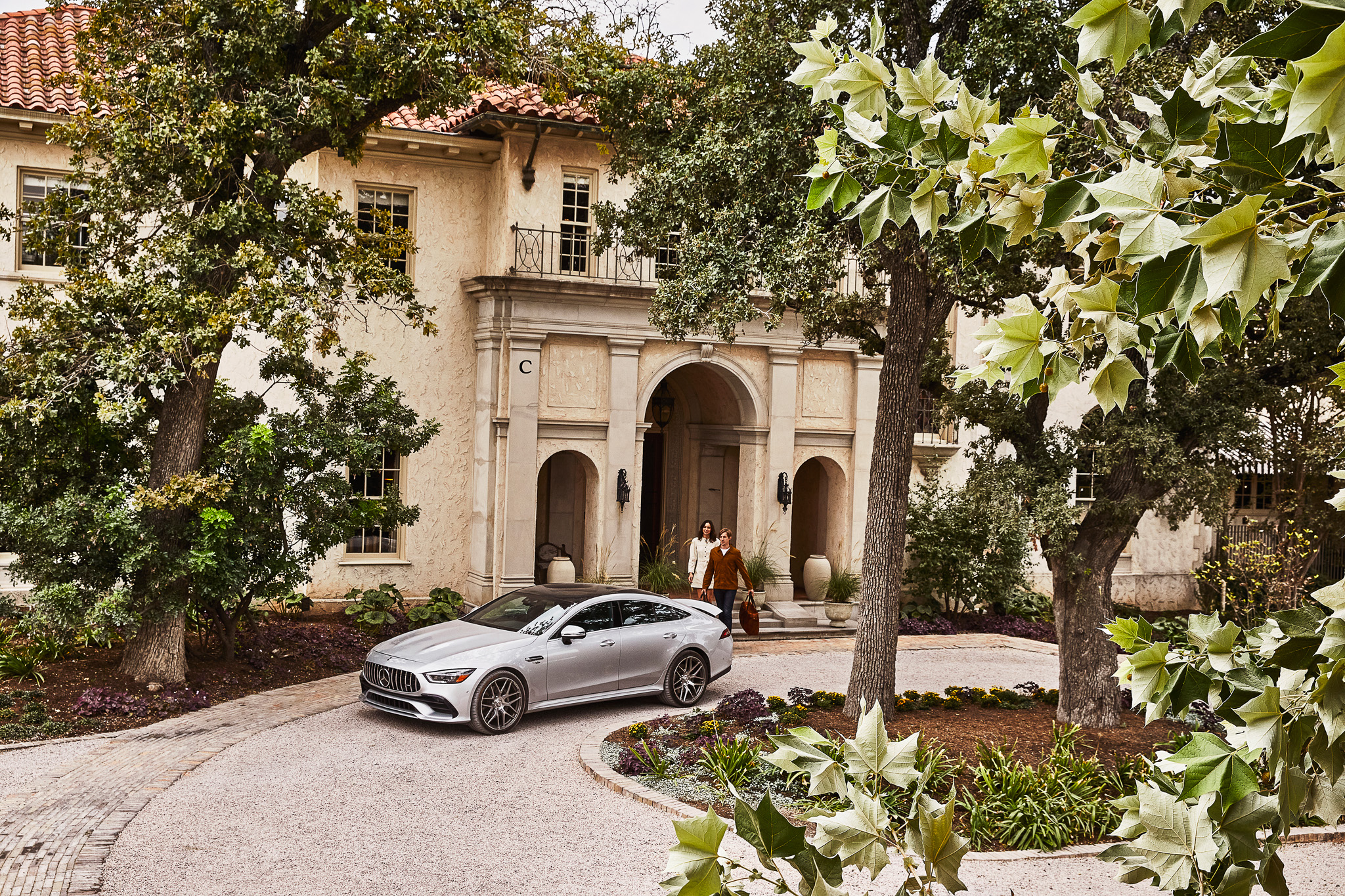 A Mercedes Benz sits in the round about driveway at this bespoke location with lush foliage.