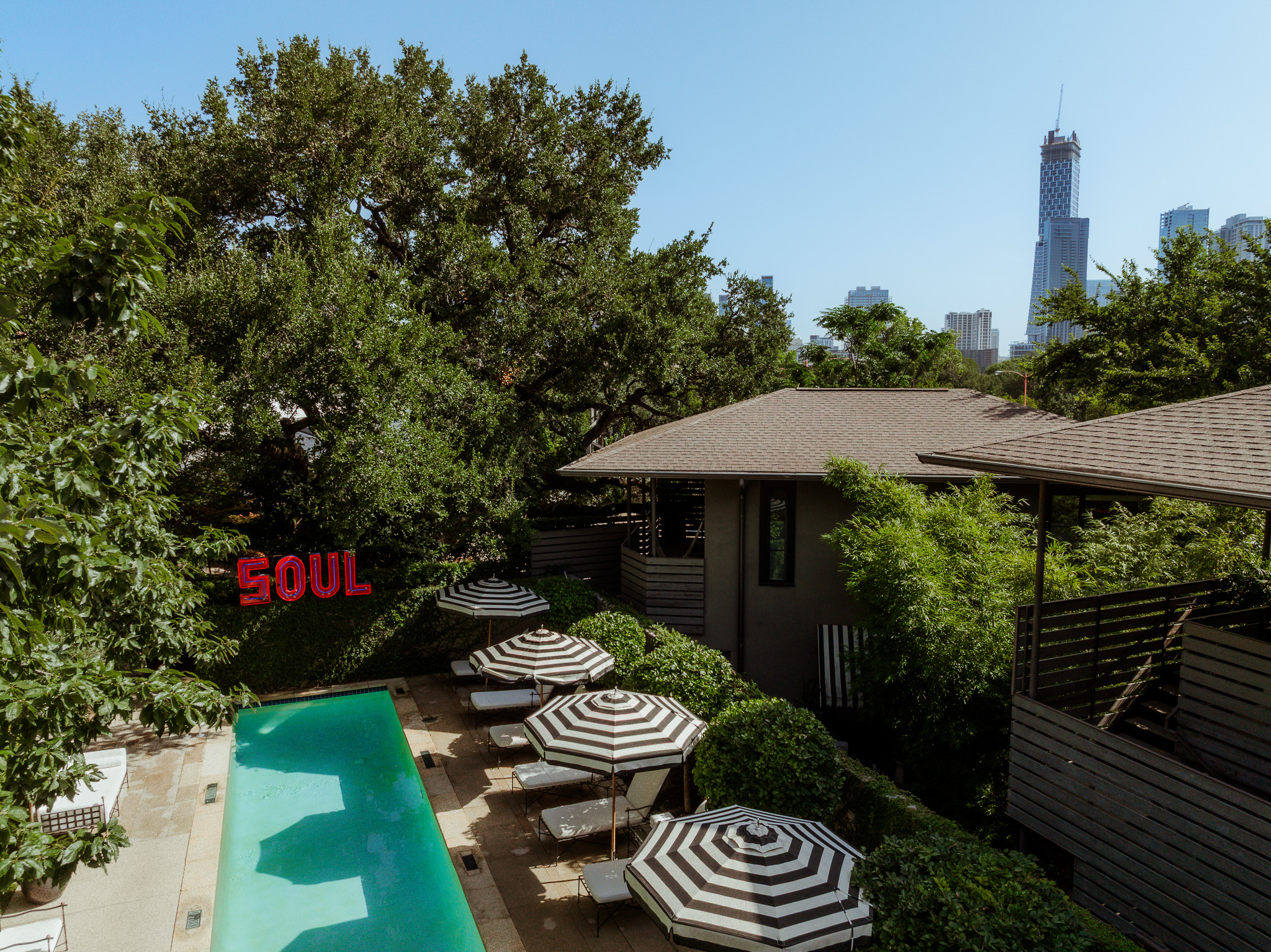 This image shows a pool with lounging pool chairs splayed out at The Hotel St. Cecilia. The Austin Skyline can be seen peering above the neighboring buildings in the top right of the image.