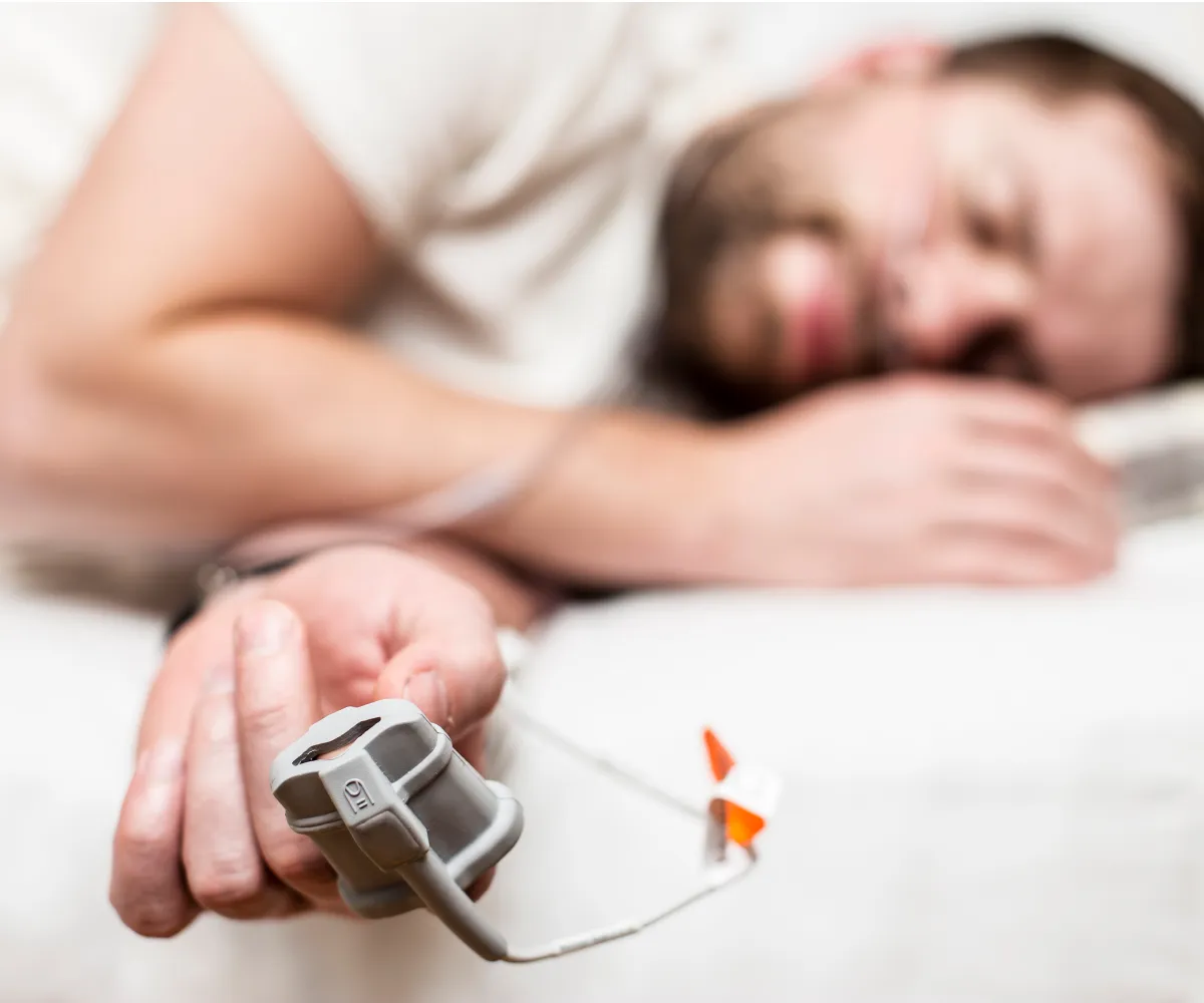 A man sleeps on his side, wearing an oxygen saturation monitor on his finger.