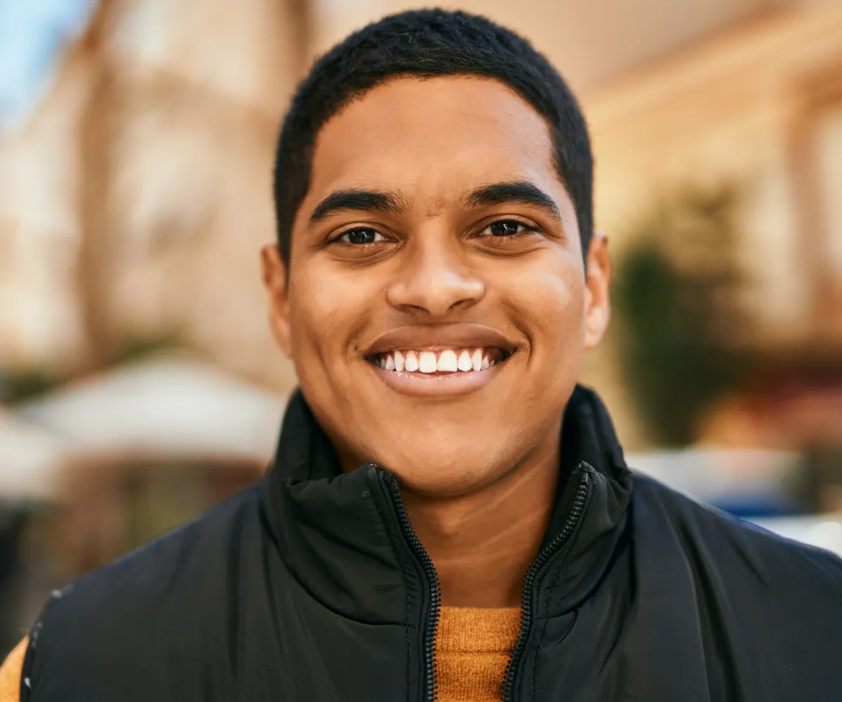 A person smiles warmly while standing outdoors.