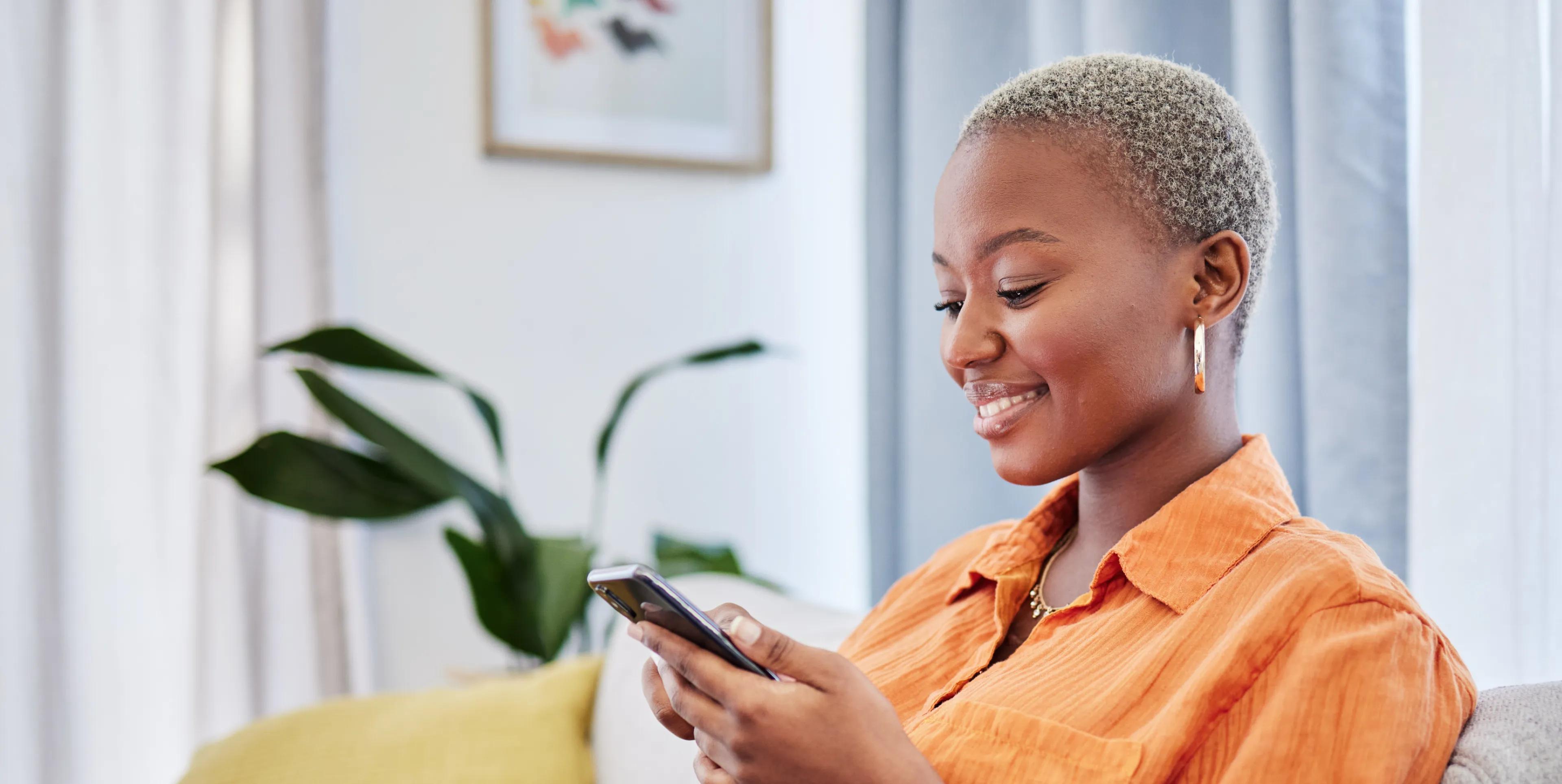 A person in an orange shirt smiles while using a smartphone indoors.