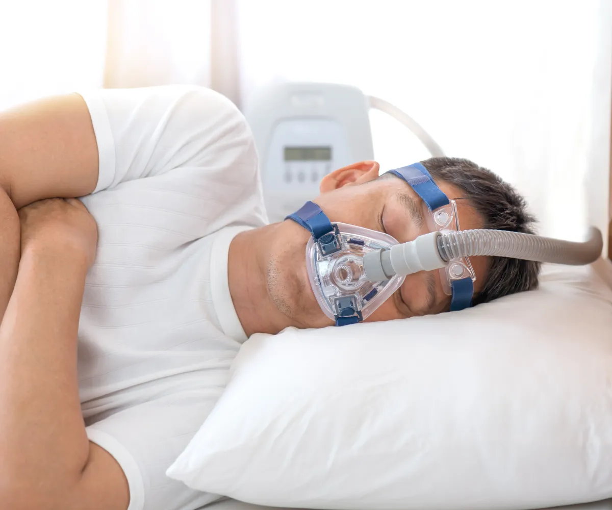 A person sleeps on their side wearing a CPAP mask connected to a machine.