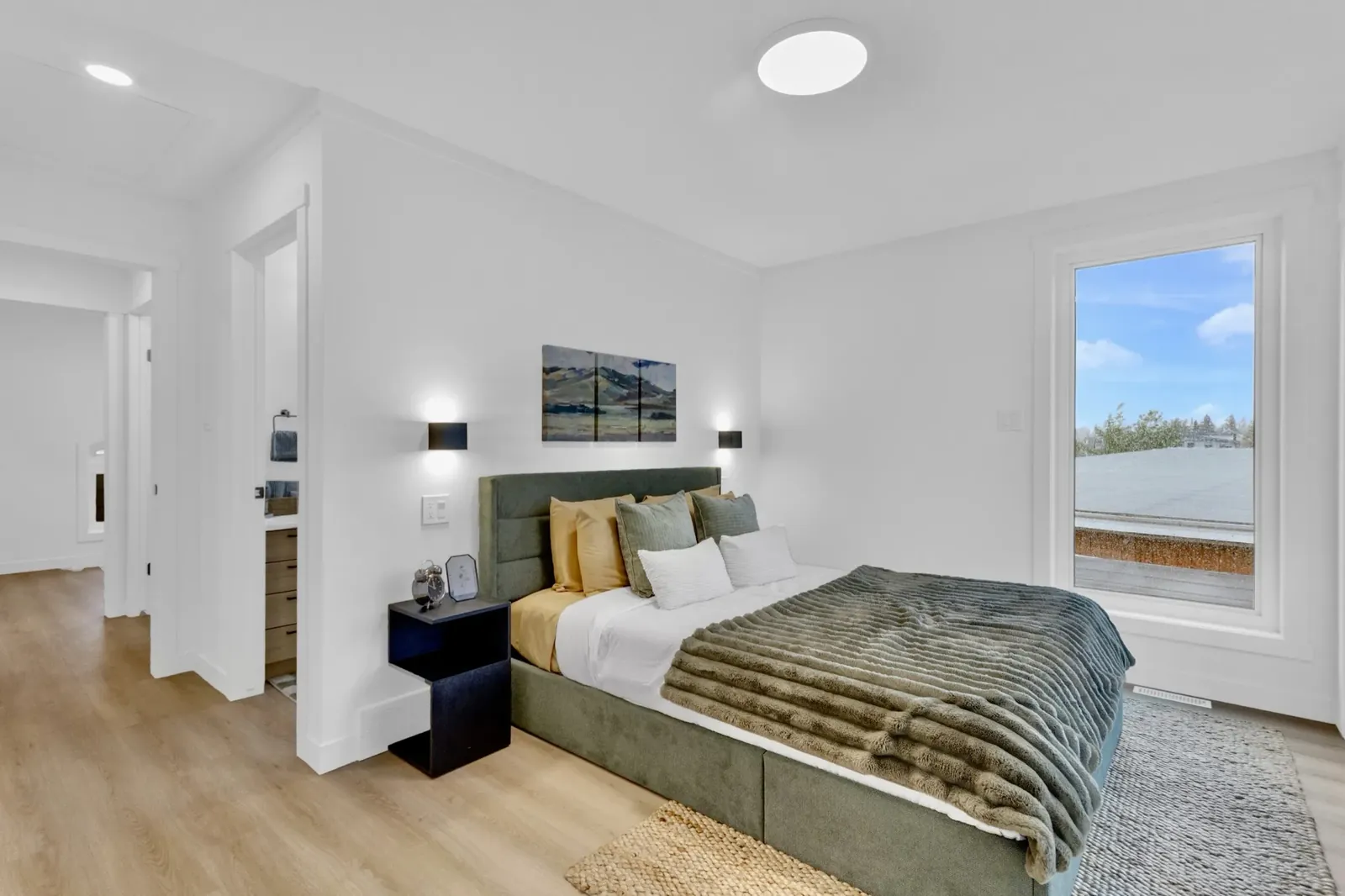 A bedroom with a green upholstered bed and a tall window onto open sky