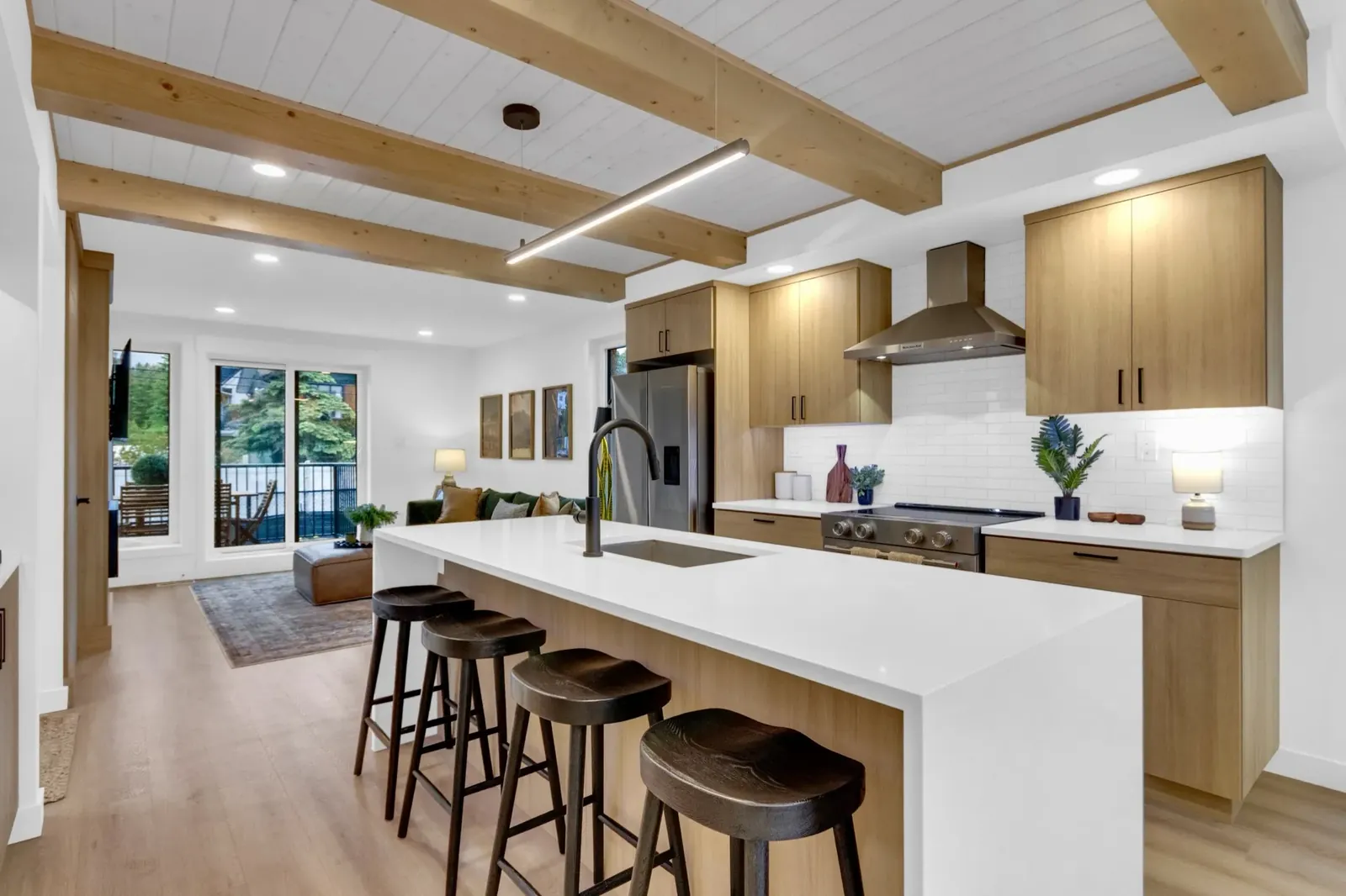 The kitchen island, beams and finished living area opening to the deck in a Colliery Parc home in South Canmore