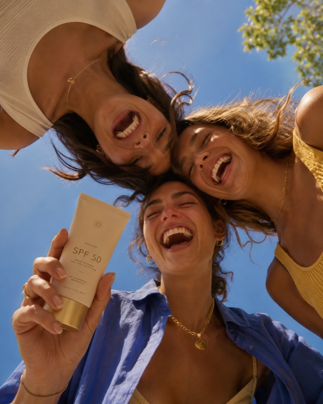 Three laughing women photographed from below against a blue sky