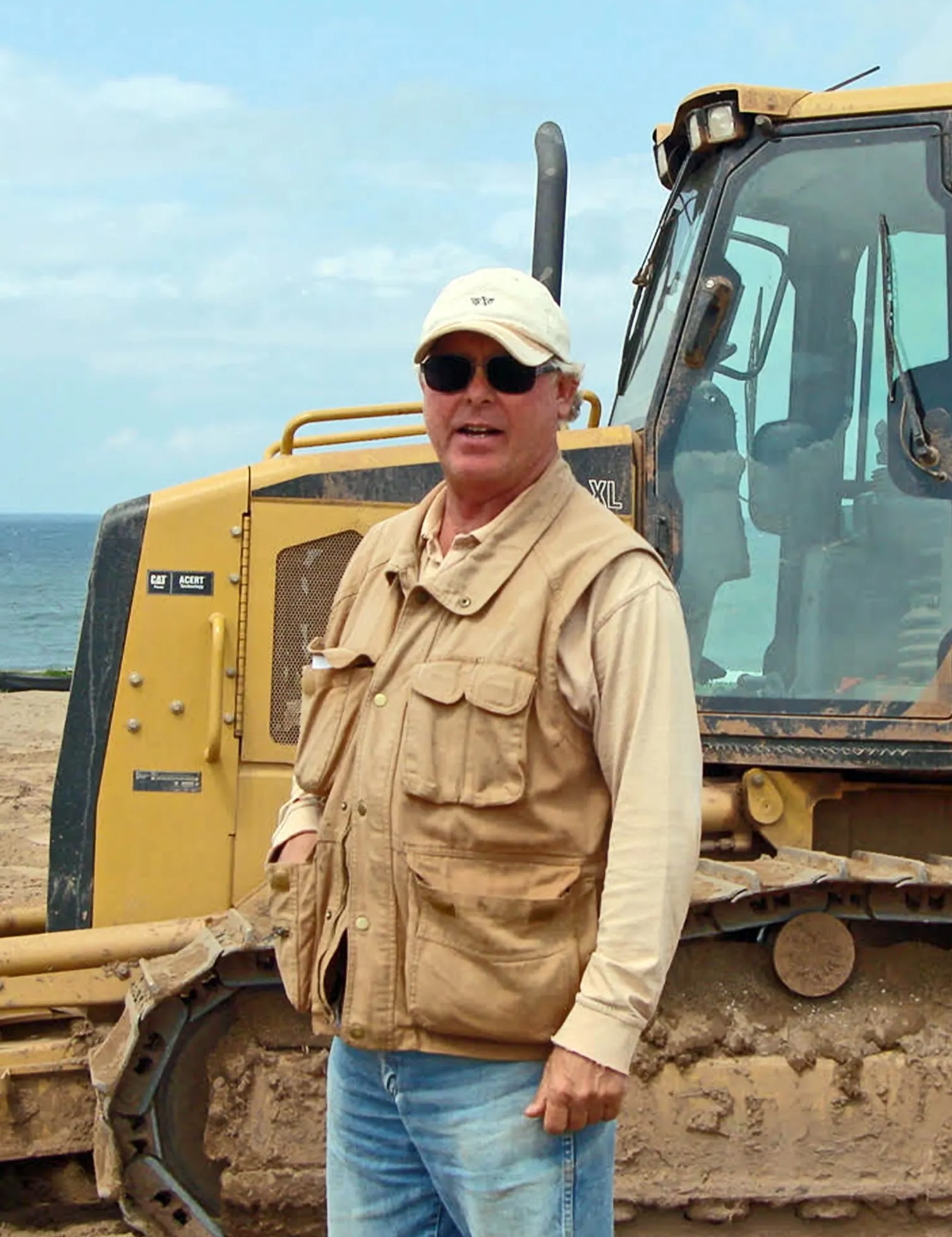 Portrait photo of Rod Whitman at Cabot Links standing in front of a bulldozer, golf course architect