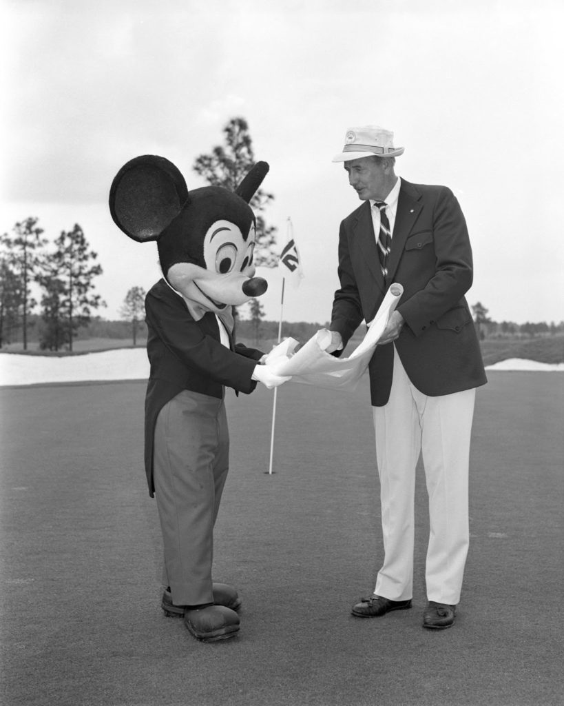 Portrait photo of Joe Lee, golf course architect standing next to Mickey Mouse
