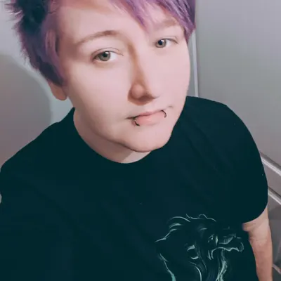 Personne avec des cheveux courts violet, portant un t-shirt noir avec des piercings aux lèvres.