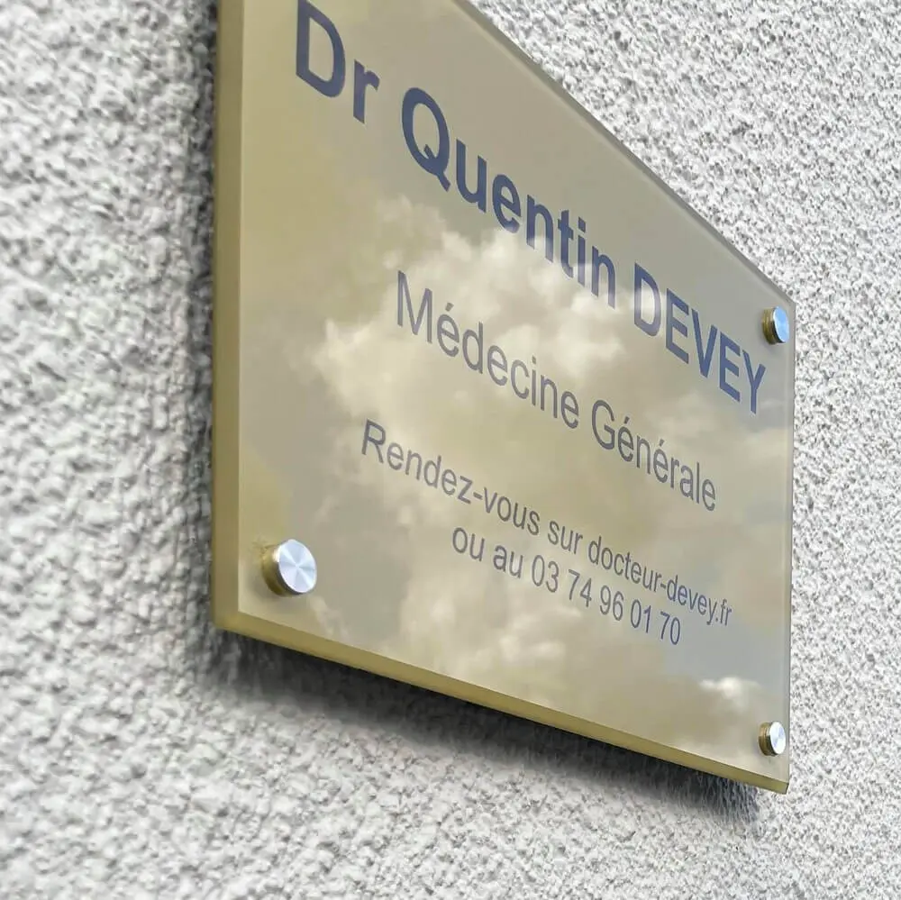 Plaque dorée fixée sur un mur en crépi indiquant Dr Quentin DEVEY, Médecine Générale.