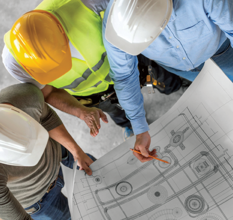 an overhead view of Three construction workers standing  and looking at blue prints. 