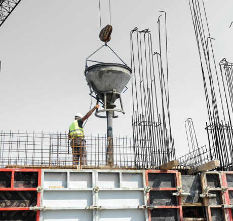 A construction worker standing on a metal structure, guiding a metal funnel attached to a crane. 