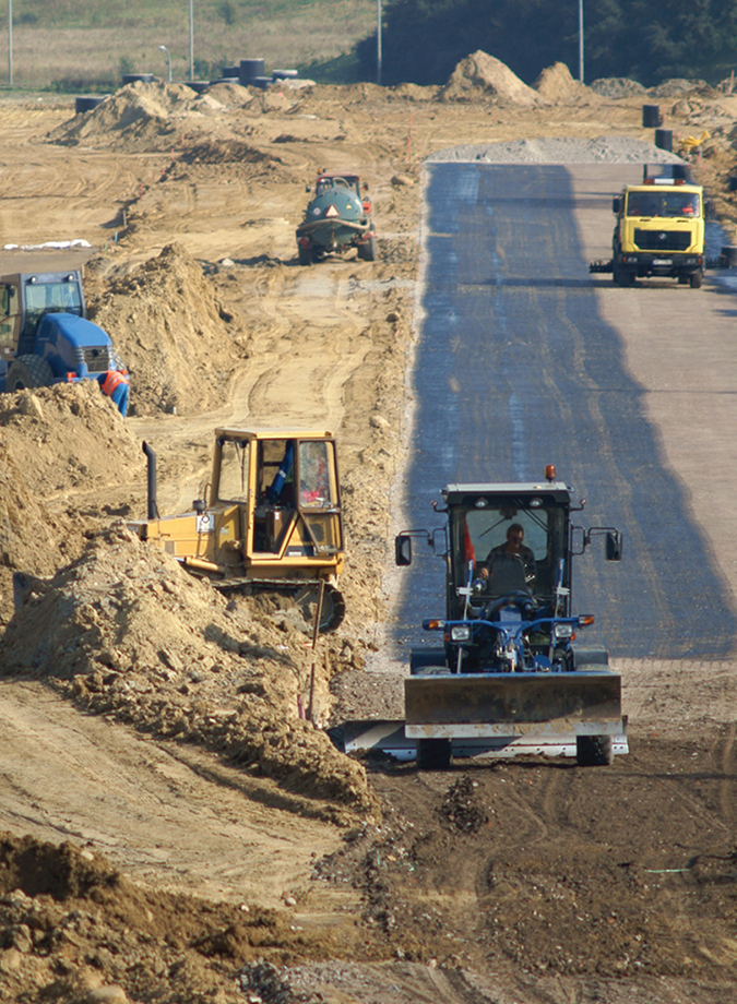 Five heavy machinery working on a long stretch of dirt road 