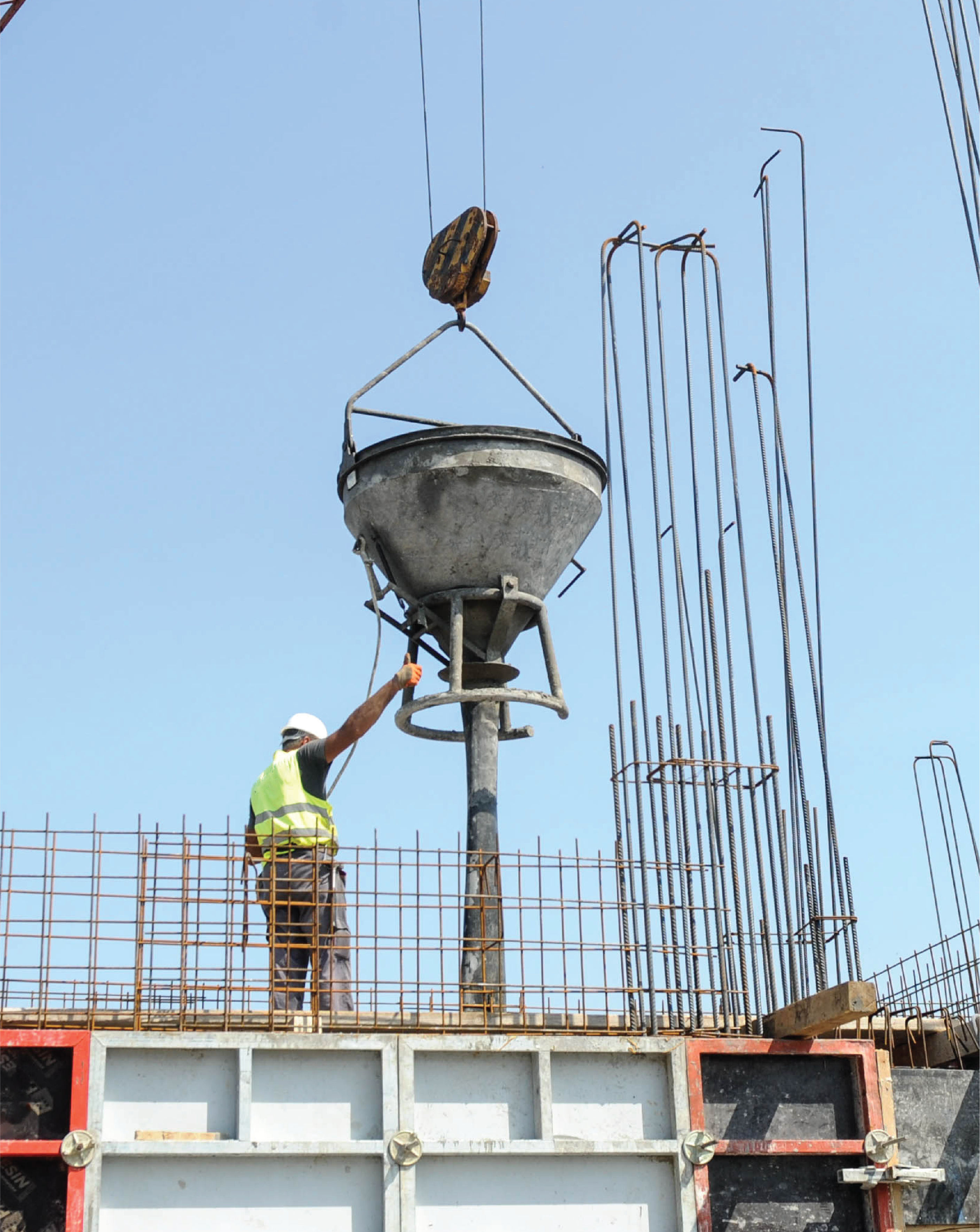 A construction worker standing on a metal structure, guiding a metal funnel attached to a crane. 