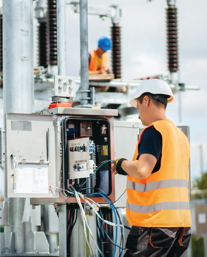 An electrician working on a electrical box. They are wearing a high-vis and a hard hat 