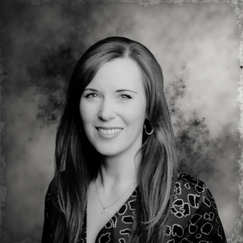 Black and white portrait of a smiling woman with long hair wearing hoop earrings and a patterned blouse.