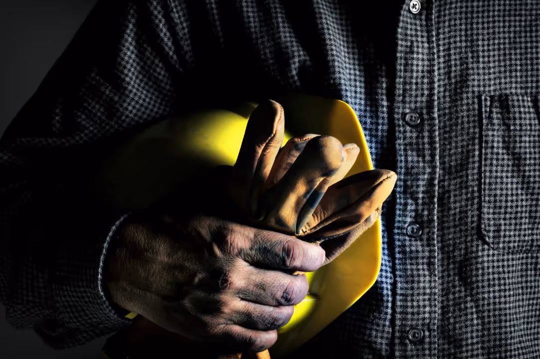 HVAC operator is plaid shirt holding his hardhat and work gloves tightly.