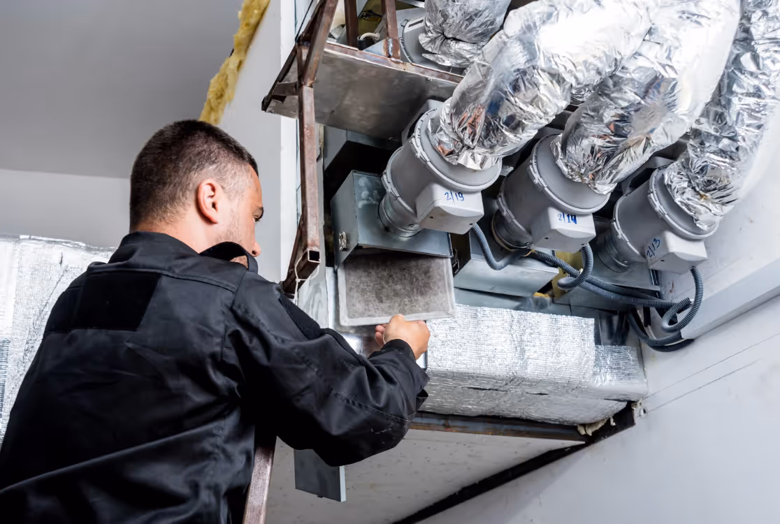 HVAC technician servicing an air handler inside a mechanical room.