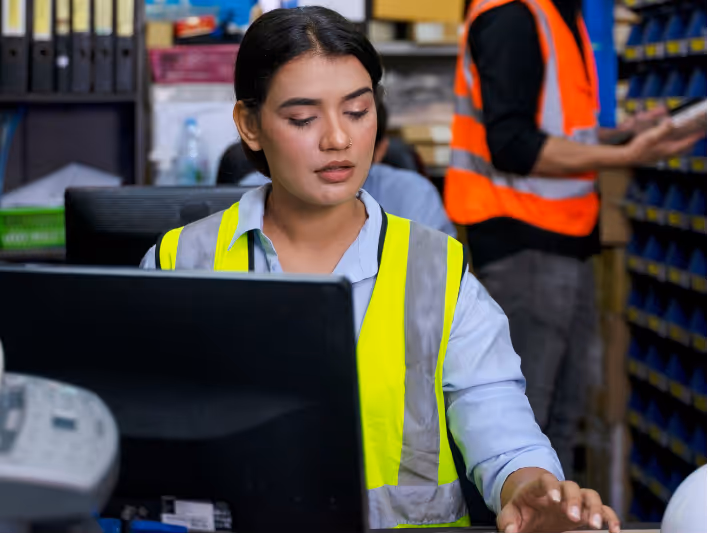 HVAC sales executive Erica reviewing job files in a parts room while a technician pulls inventory behind her.