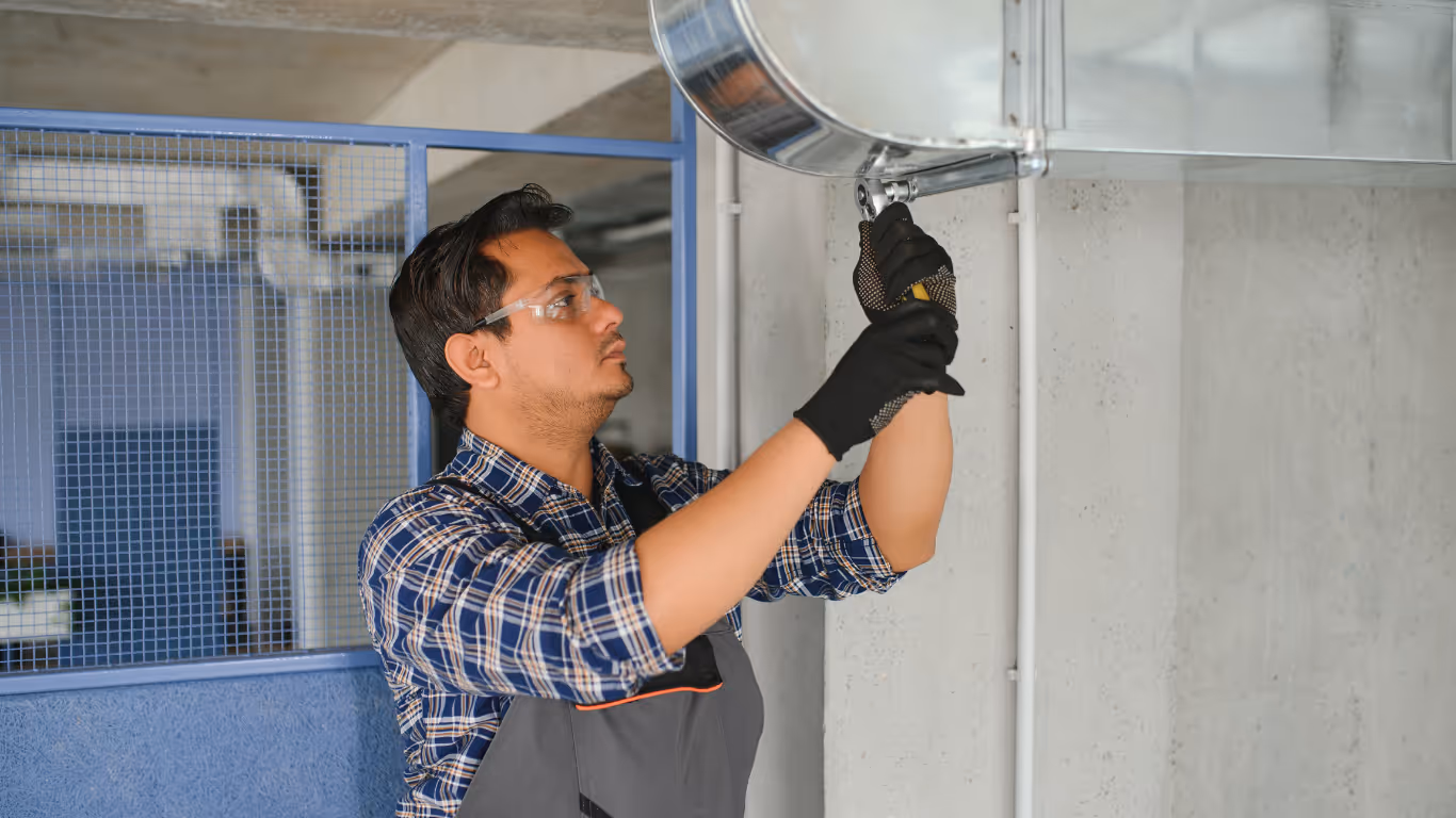 Commercial HVAC technician adjusting metal ductwork inside a commercial building.