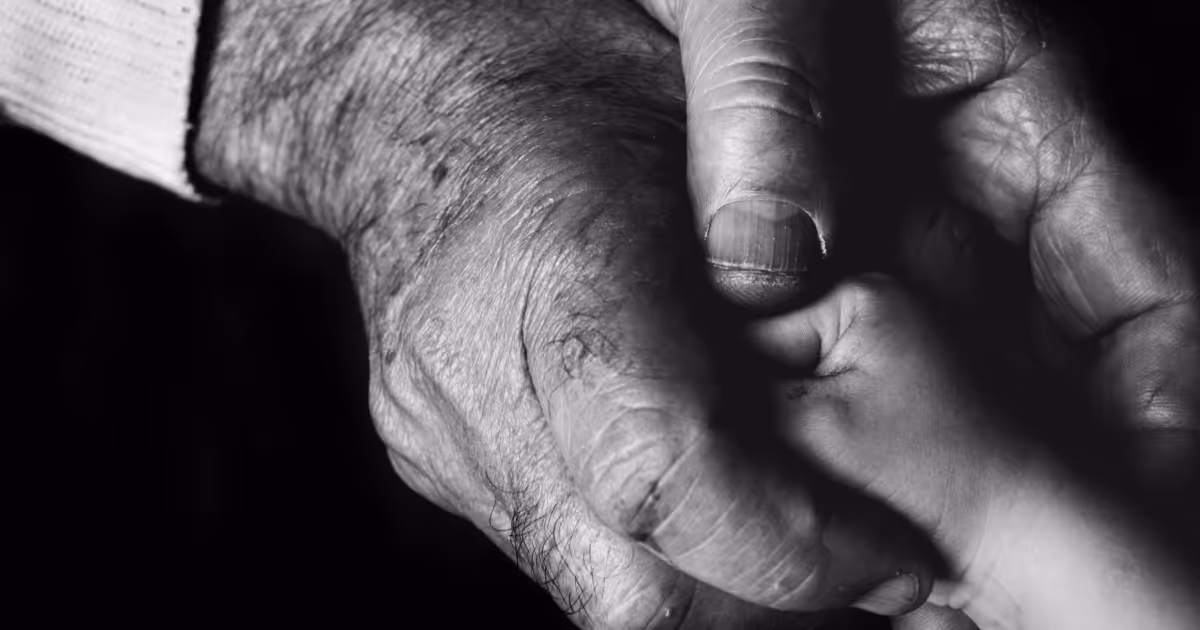 A close-up black and white shot shows an older person's wrinkled hand holding a child's smaller hand.