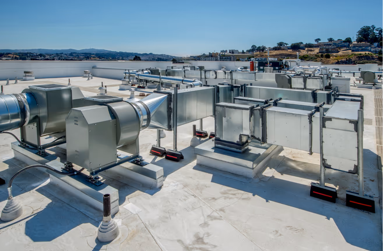 A rooftop HVAC system with large metal ducts and fans under a clear blue sky.
