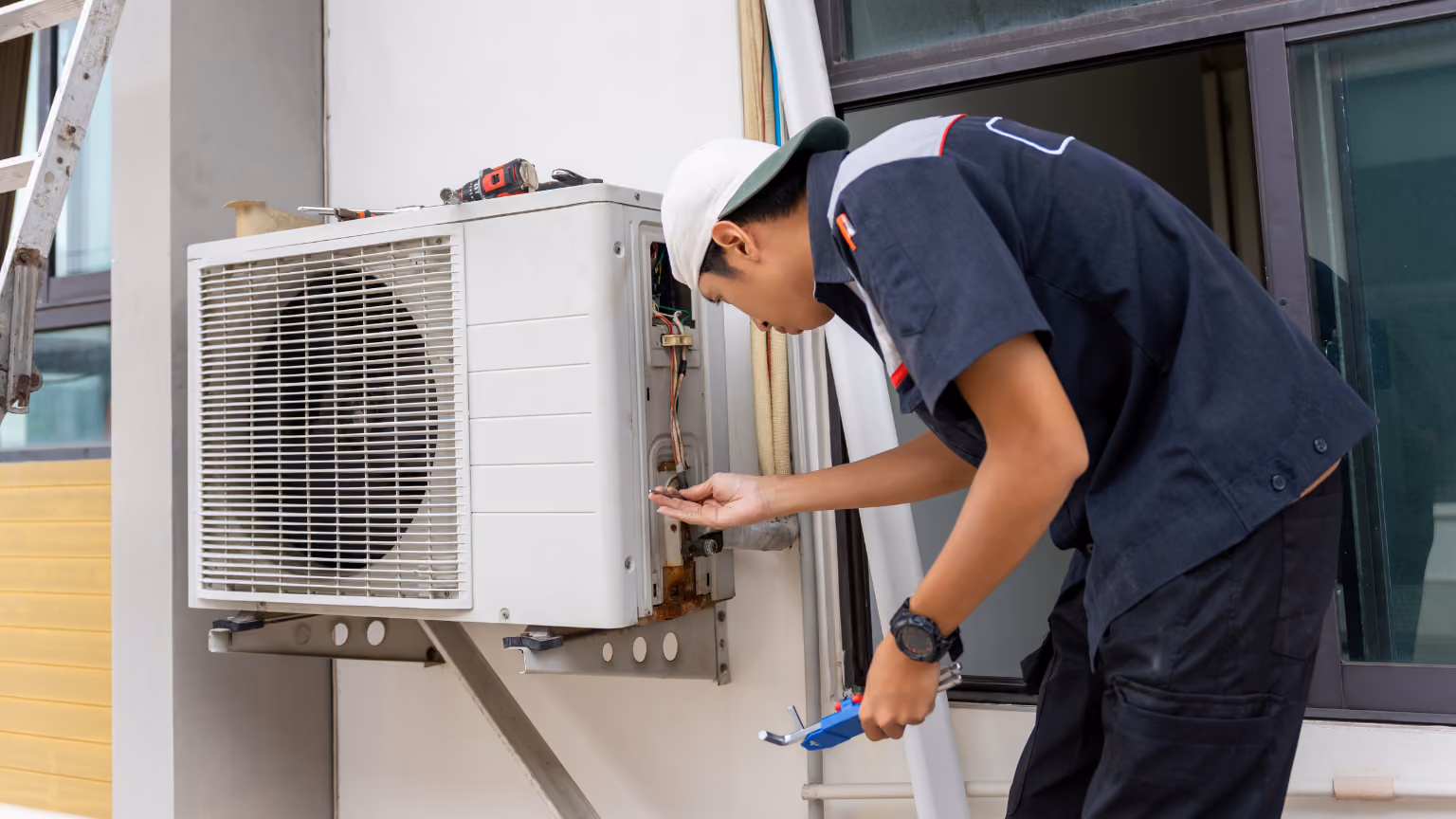 An hvac tech in a hard hat and reflective vest holds a clipboard while standing in front of an industrial air conditioning unit.