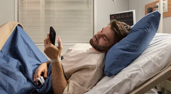 A man in a hospital bed, using his smartphone to stay connected during his recovery