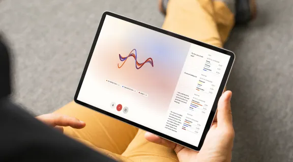 Person holding a tablet displaying a voice emotion analysis interface with a colorful waveform and emotional metrics like determination, concentration, and anger.