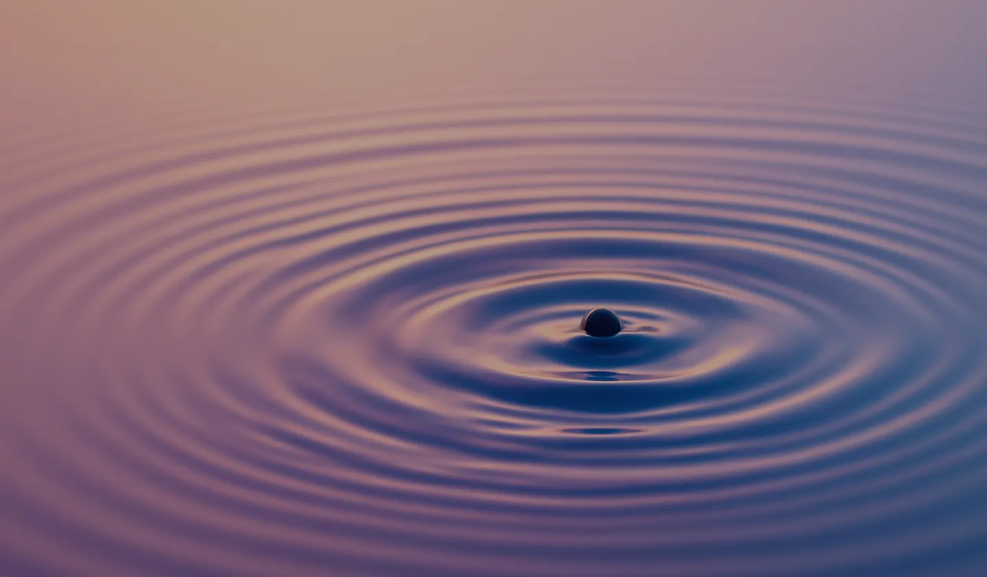 Water droplet creating concentric ripples on a calm reflective surface with purple and pink hues.