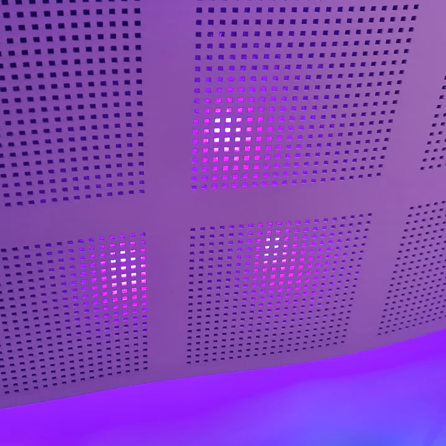 Close-up of perforated acoustic ceiling tiles with integrated purple LED backlighting, designed for both aesthetic impact and high-performance sound absorption in a modern interior.