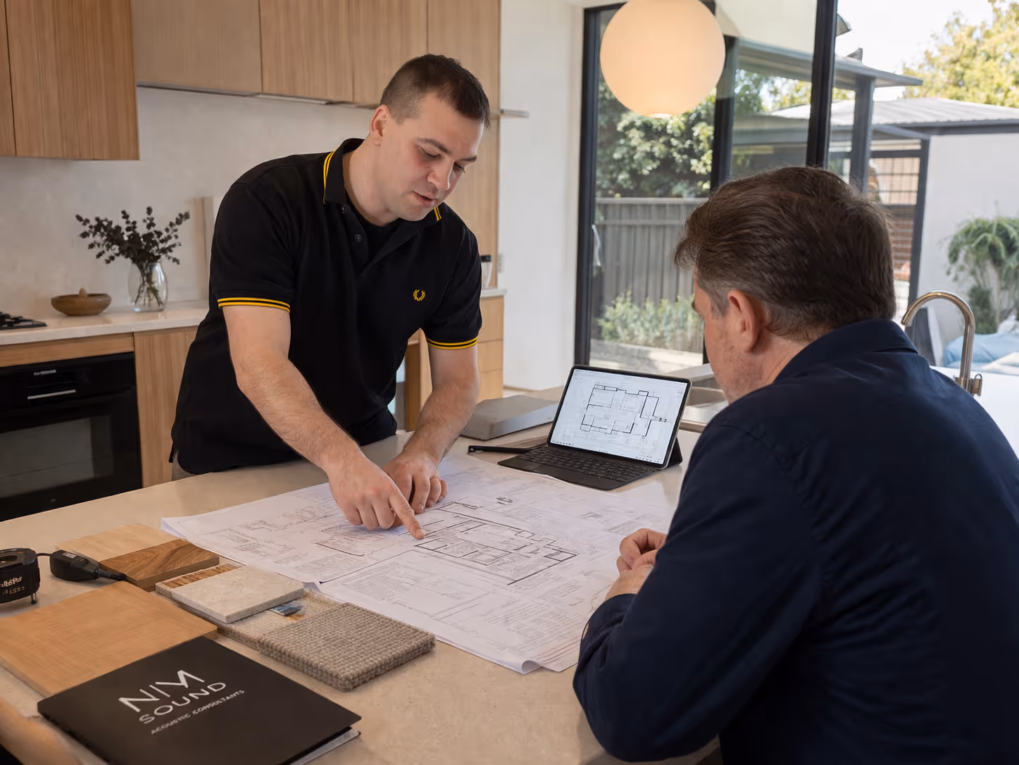 Nicholas Marriott providing an architectural acoustics consultation. Features technical blueprints, material samples, and a digital tablet for integrated project leadership.