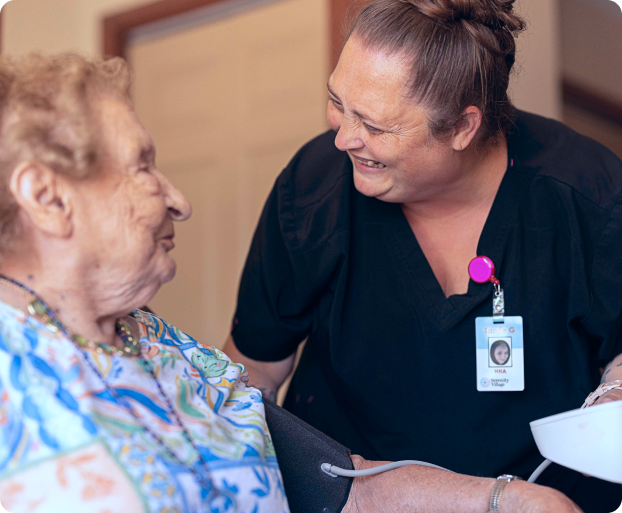 Caregiver smiling and taking blood pressure of elderly woman in a home setting.