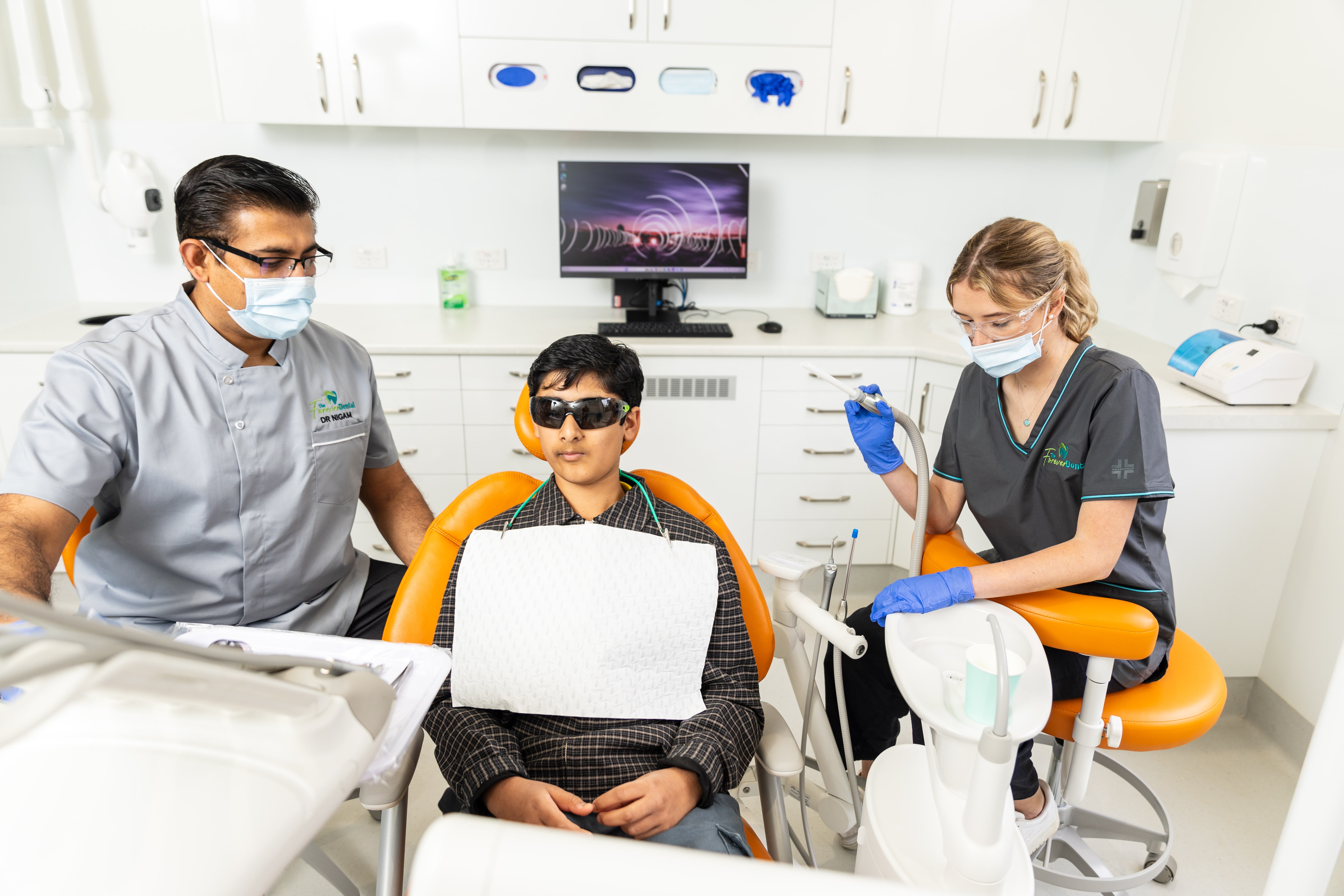 Dr. Nigam performing a dental procedure on a young patient with the support of a dental assistant at The Forever Dental & Smile Centre.