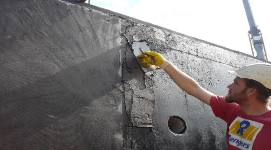 Construction worker in a white helmet applying cement plaster to a wall with a trowel.