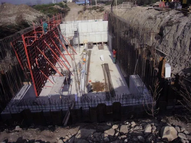 Construction site showing concrete foundation with metal rebar and scaffolding on one side.
