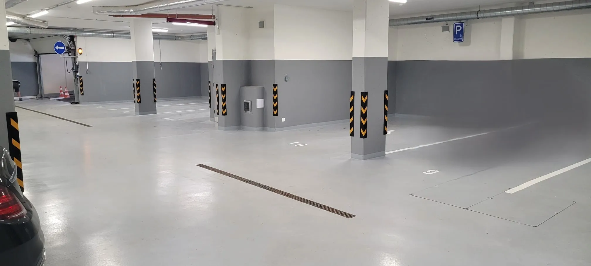 Empty indoor parking garage with gray and white walls, pillars with black and yellow hazard stripes, and marked parking spaces.